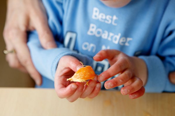 Ein Kind öffnet mit den Händen eine Orange und erhält Unterstützung